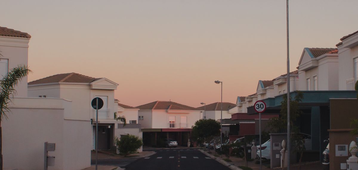 A suburban street at dusk under a clean gradient sky, houses going quiet
