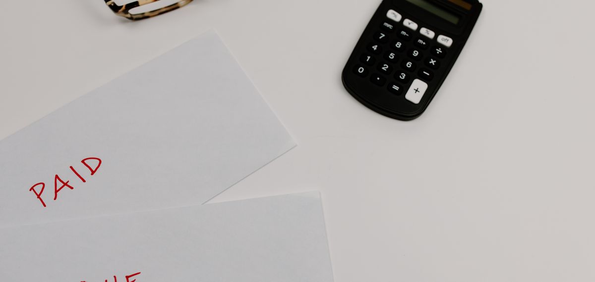Two envelopes marked paid and due beside a calculator and reading glasses on a desk