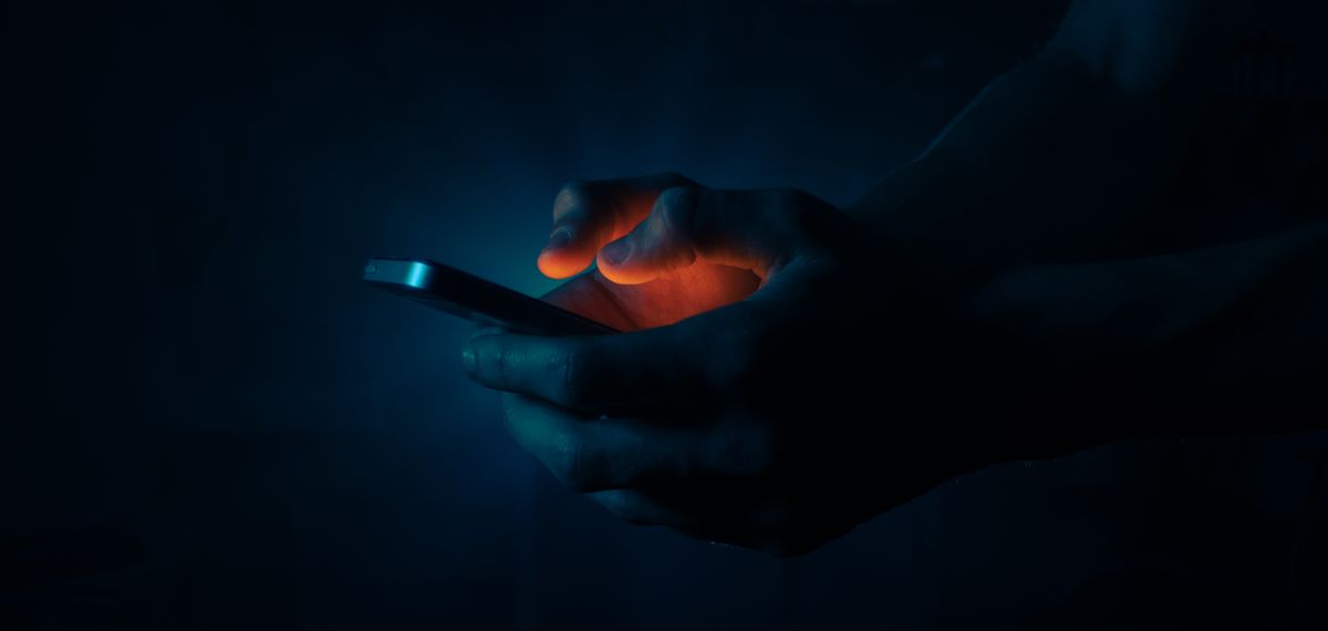 Hands holding a glowing phone in the dark