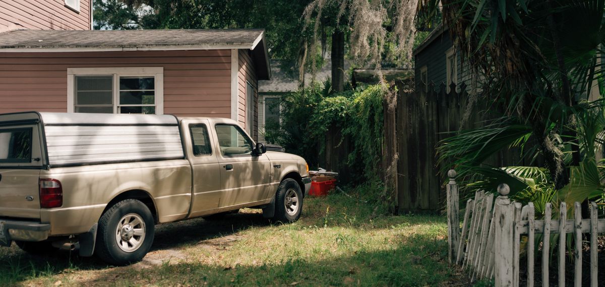 A work pickup truck parked beside a house, yard and fence in summer light